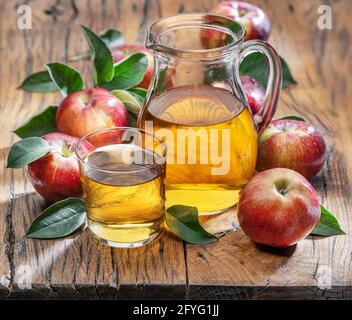 Glass and carafe of fresh apple juice and organic apples on dark old wooden table. Stock Photo