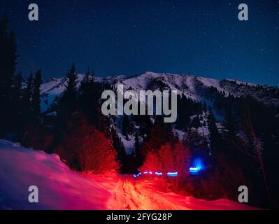Abstract beam of red and blue glowing lights on the road at winter snowy forest in the mountains under night sky with stars Stock Photo