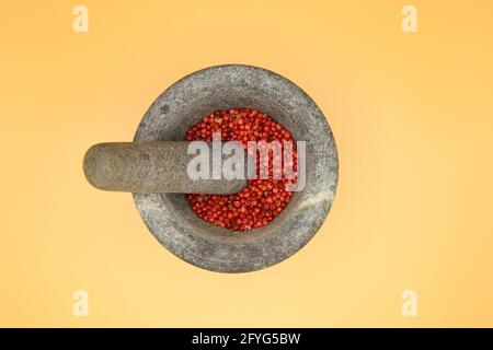 Top view close up on isolated gray basalt stone mortar with pestle and red pepper corns, yellow blank background (focus on center) Stock Photo