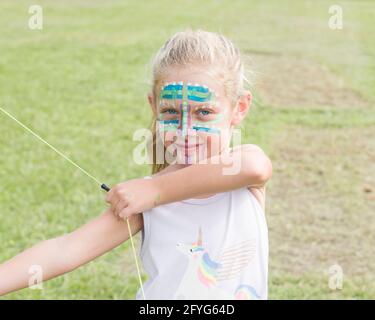 6 year old girl with a bow (and arrow).  Her face is painted like an Indian. Stock Photo