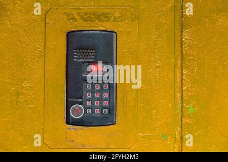 An intercom on old painted yellow steel surface with a keypad, digital display and rfid sensor for calling close-up. Stock Photo