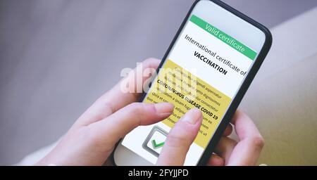Composition of woman holding smartphone with covid 19 international certificate of vaccination Stock Photo