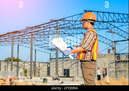Engineer standing on a building site looking at building blueprint, Thailand Stock Photo