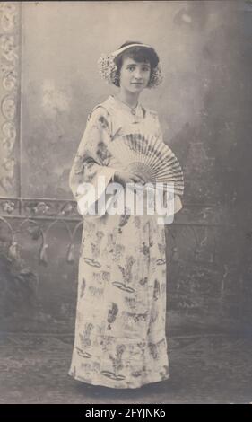 Vintage photographic postcard showing a girl dressed up in a Japanese kimono and holding a fan. Stock Photo