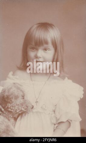 Vintage early 20th century photographic postcard showing a beautiful young girl holding a teddy bear. Stock Photo