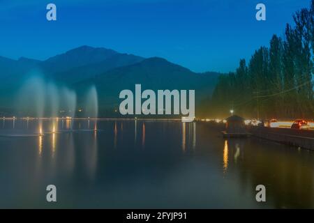 Fountains over the Dal Lake with mountains in the background, at dusk. Dal Lake is the most famous lakes of Jammu and Kashmir, India and is famous. Stock Photo