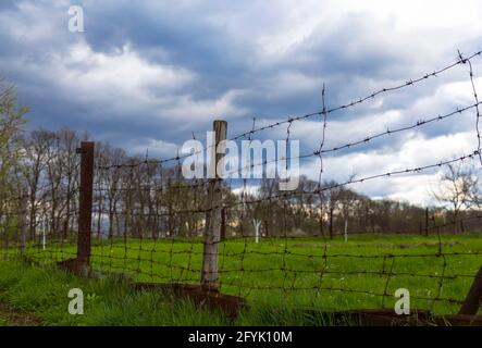 The division of green grass and black earth stretches an old barbed wire fence. Rusty barbed wire, division into black and white Stock Photo