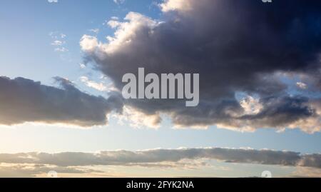 Heavy dark clouds on colorful blue sky background, space. Cloudscape at sunset, sunrise concept. Sunbeams through the clouds form image of an angry wi Stock Photo