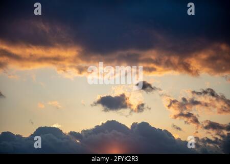 Colorful sunset and dark cloudy sky. Sunrise blue gray orange yellow color heaven, sunbeams through heavy clouds background, space. Dramatic abstract Stock Photo