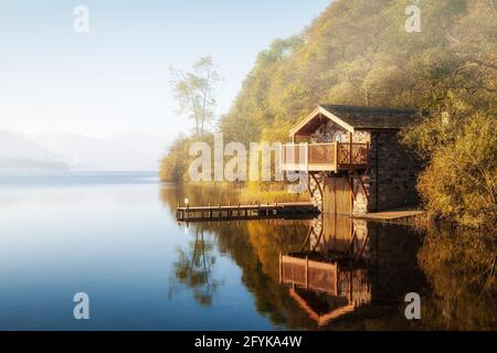 An idyllic autumn scene of the Duke of Portland boathouse at Ullswater in the Lake District National Park, with the early morning mist clearing fast. Stock Photo