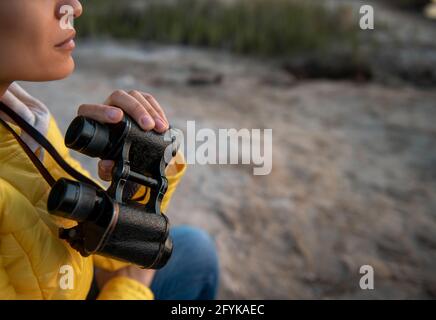 Focus on old binoculars in the hand of a young woman enjoying the beautiful view of the nature. Closeup Stock Photo