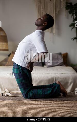 Sporty young african man working out, yoga, pilates or fitness training, standing in asana ushtrasana Stock Photo