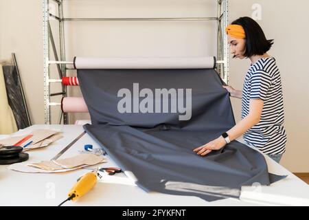 Young tailor take roll of fabric to cur pattern textile measure working on new collection in atelier Stock Photo