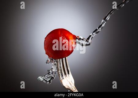 Cherry tomato on a fork is poured with water on a black and white background Stock Photo