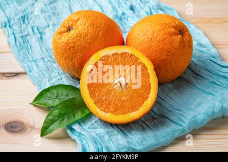 Ripe sweet juicy oranges on a turquoise cloth over wooden table. Two whole and one half of fresh citrus fruits. Healthy eating, organic vitamin C. Stock Photo