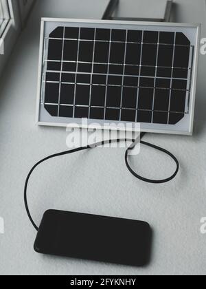 Portable solar panel on the windowsill is generating energy and charging the smartphone. Alternate sources of energy Stock Photo