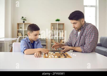 Portrait of concentrated father and son playing checkers sitting at home table Stock Photo