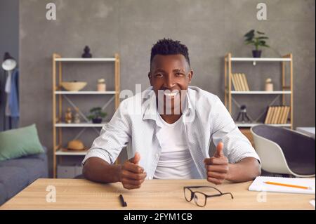 Happy friendly young African man sitting at table in home office and smiling at camera Stock Photo