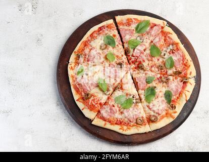 Pizza with ham and olives on a round wooden cutting board on a light gray background. Top view, flat lay Stock Photo