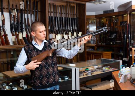 Interested adult man examining pump action hunting rifle before buying in modern gun shop Stock Photo