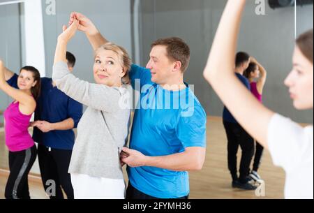 Smiling middle aged woman practicing bachata movements in dance studio for adults Stock Photo