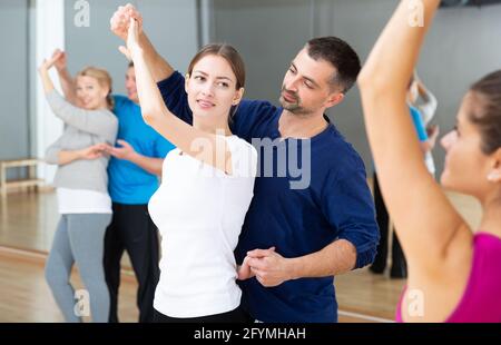 Young smiling woman and man practicing social dance moves in pair during group class Stock Photo