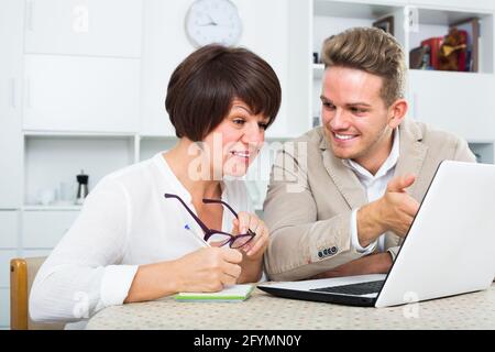 Mother and young son consider new software on laptop sitting at table Stock Photo