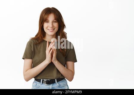 Image of thoughtful sly girl smiling, steeple fingers and looking at camera, having interesting idea, planning and scheming, standing against white Stock Photo