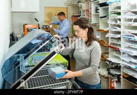 Female worker packs notebooks in a vacuum packing Stock Photo