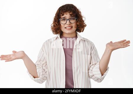 Sorry I dont know. Clueless young woman student in glasses shrugging shoulders puzzled, smiling awkward as have no idea, cant help, nothing to say Stock Photo