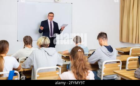 Man teacher with notebook is giving interesting lecture for students in the classroom Stock Photo