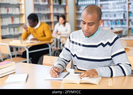 Portrait of young adult man studying in at public library Stock Photo