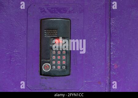 An intercom on purple painted red steel surface with a keypad, digital display and rfid sensor for calling close-up. Stock Photo