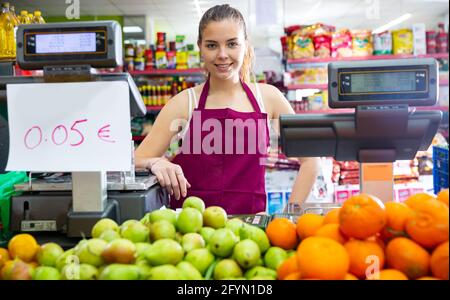 Portrait of young female shop assistants laying out and weighing fruit and vegetables on scales in grocery shop Stock Photo