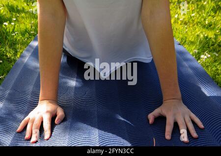 Woman wearing a white t-shirt practicing yoga on a blue mat on the green grass in the upward facing dog position outdoo Stock Photo
