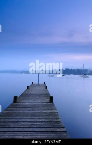 View from small wooden jetty (boat moorings, calm water, boardwalk, dramatic blue hour evening light) - Windermere, Lake District, Cumbria England UK. Stock Photo