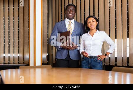 Smiling African American man wearing business suit and stylish Hispanic woman standing in modern interior on meeting room. Concept of successful busin Stock Photo