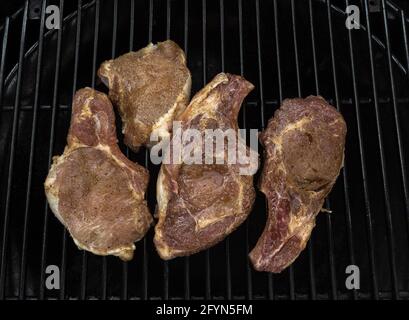 Four juicy half-roasted pork chops on a gas grill Stock Photo