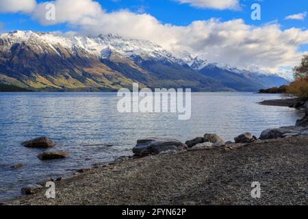 Lake Wakatipu in the South Island of New Zealand. A rocky beach in the foreground, with the mountains of the Southern Alps on the horizon