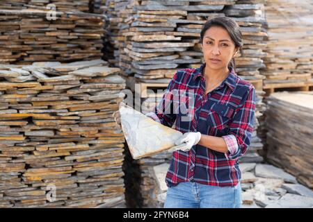 Positive hispanic woman worker posing with natural stone tile at building materials warehouse Stock Photo