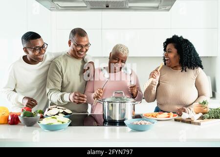 Happy black family having fun cooking together in modern kitchen - Food and parents unity concept Stock Photo