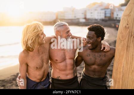 Happy fit surfers with different age and race having fun surfing together at sunset time - Extreme sport lifestyle and friendship concept Stock Photo