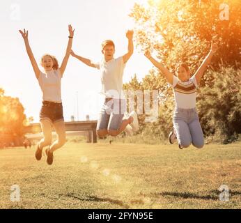 Portrait of cheerful teenage girls and guy jumping together in summer city park. Concept of happy adolescence Stock Photo