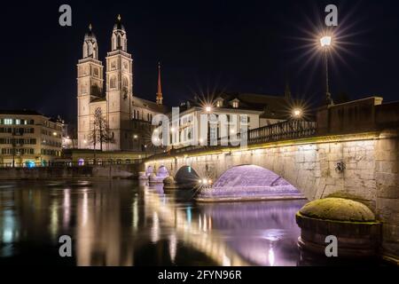 Munsterbrucke and Grossmunster church reflecting at night in river Limmat, Zurich, Switzerland Stock Photo