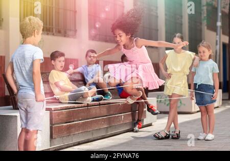 Smiling mexican girl playing rubber band jumping game with european friends and laughing outdoor Stock Photo