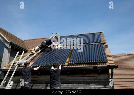 Heating engineer installing evacuated solar thermal collecting tubes on south facing roof of Ecohouse in Cotswolds UK Stock Photo