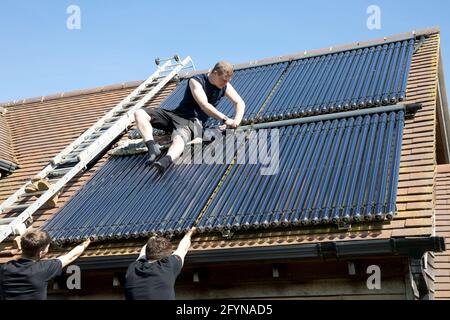 Heating engineer installing evacuated solar thermal collecting tubes on south facing roof of Ecohouse in Cotswolds UK Stock Photo