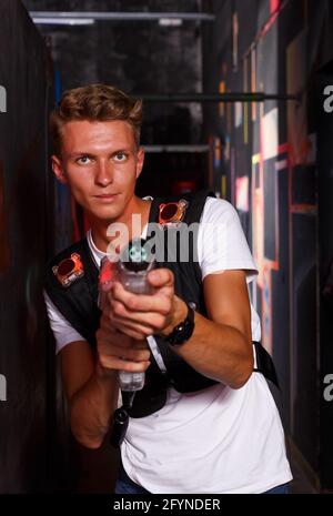 positive young guy took aim colored laser guns during laser tag game in labyrinth Stock Photo
