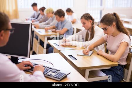 Multiracial group of teenage students working at class, listening explanations of teacher in classroom Stock Photo