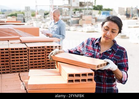 Latin american female worker holding redbricks at warehouse of building materials Stock Photo